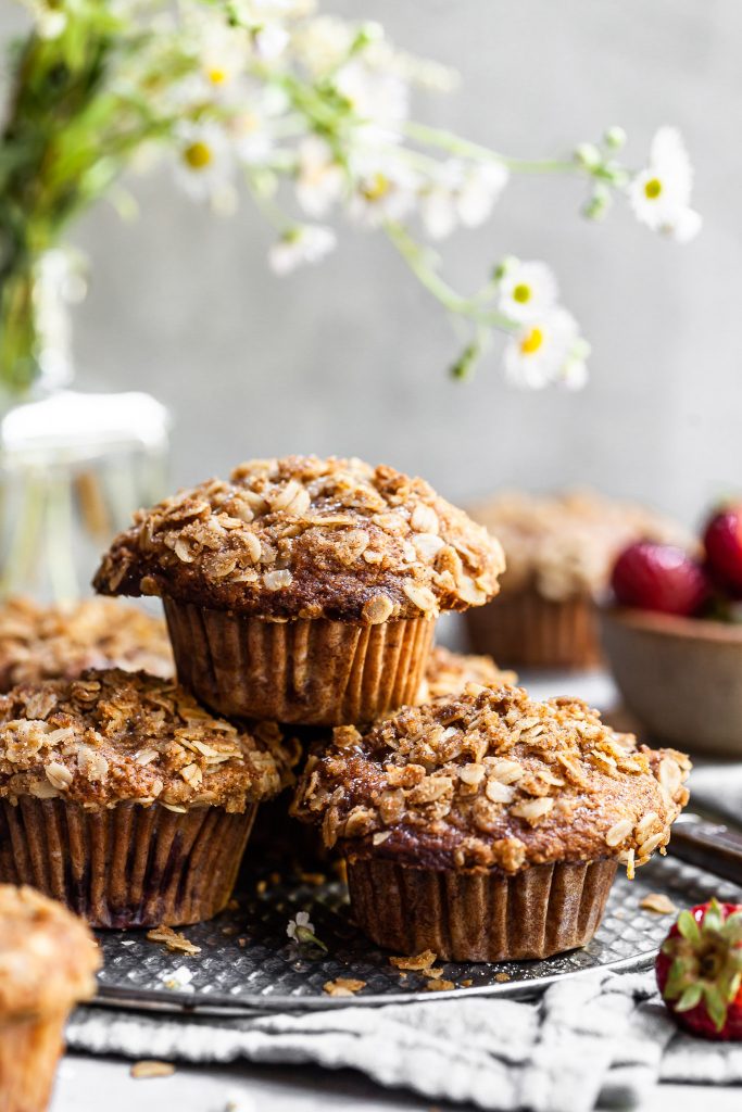 Stack of oat topped muffins on a grey platter with a bowl of strawberries in the background