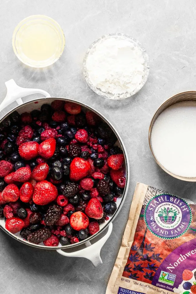 White pot contaiing frozen berries sits beside a bowl of sugar, cornstarch and lemon juice