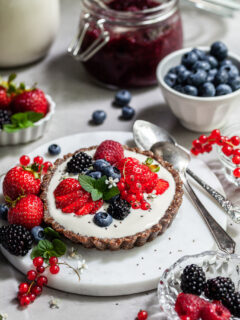 Breakfast table scene with a small tart willed with yogurt and topped with fresh berries
