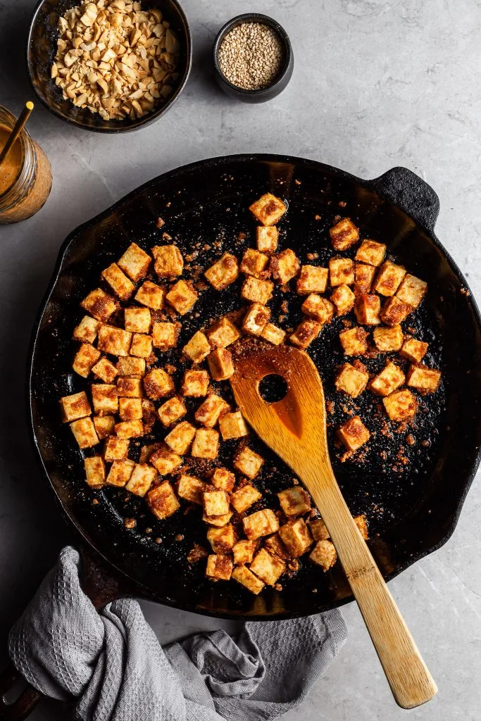 A cast iron skillet filled with cubes of crispy tofu coated in a caramelized peanut sauce