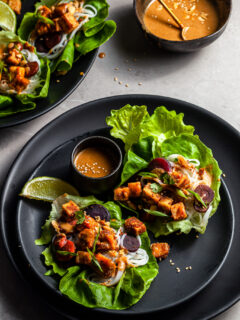 lettuce leaves on a black plate filled with tofu, rice noodles, carrots and drizzled with peanut sauce