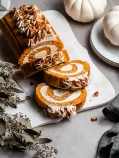 pumpkin roll on a white plater beside 2 small white pumpkins