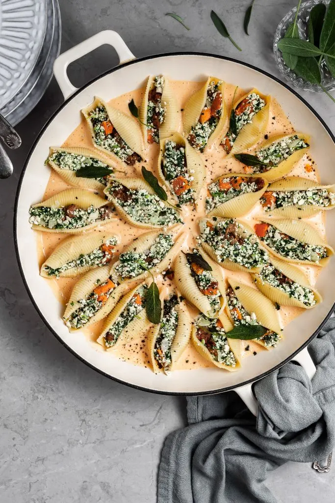 Jumbo pasta shells filled with vegan ricotta mixture are resting in a creamy sauce in a large white skillet before baking