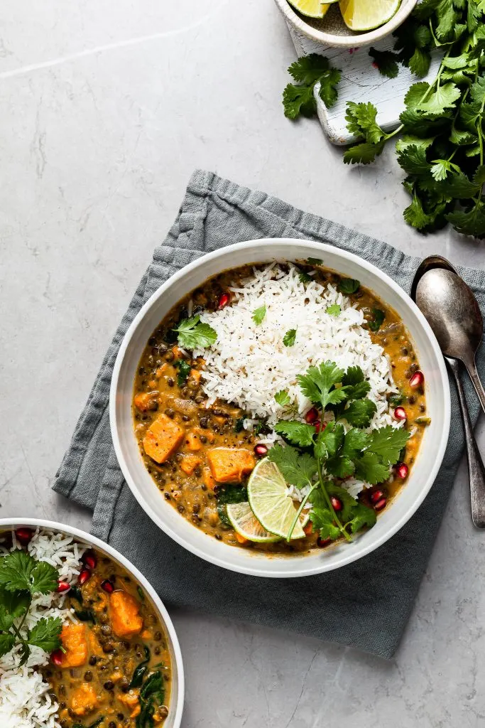 Two bowls of lentil sweet potato curry served with rice and cilantro