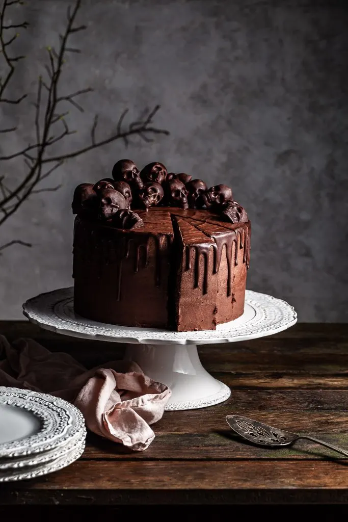 Chocolate layer cake with a chocolate ganache drip has two slices cut ready to be served with an antique spatula 