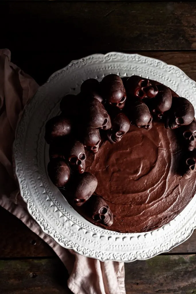 View looking down onto the top of a chocolate cake covered in chocolate ganache and decorated with small chocolate skulls arranged in the shape of a crescent moon