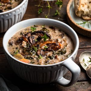 A white mug filled with creamy mushroom and rice soup with seared mushrooms garnishing the top.