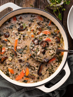 A white enamel cast iron pot filled with mushroom rice soup, being ladled out.