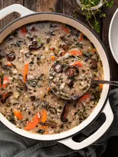 A white enamel cast iron pot filled with mushroom rice soup, being ladled out.
