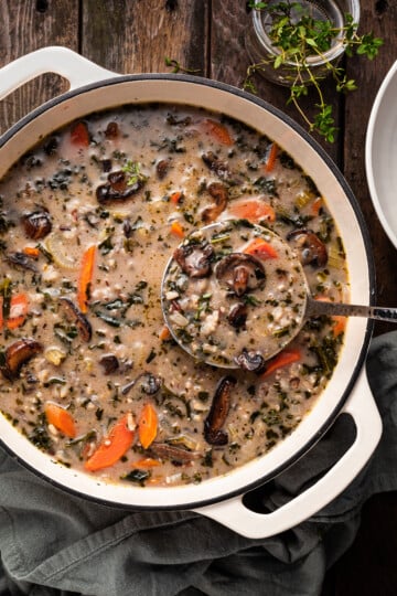 A white enamel cast iron pot filled with mushroom rice soup, being ladled out.