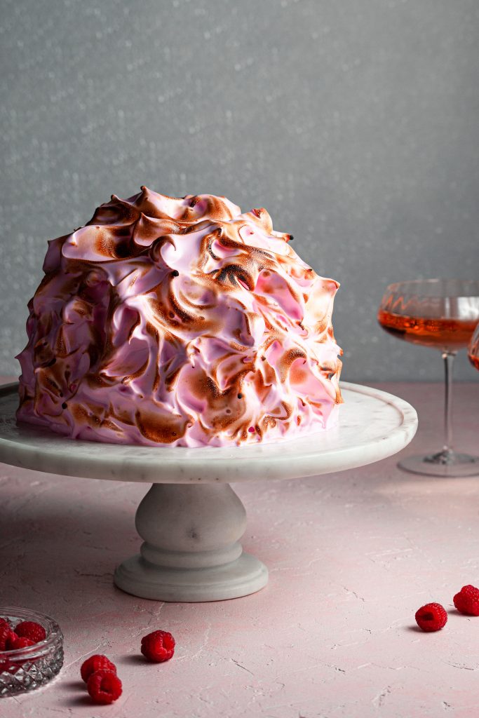 A torched bake alaska covered in pink meringue beside two glasses of rose