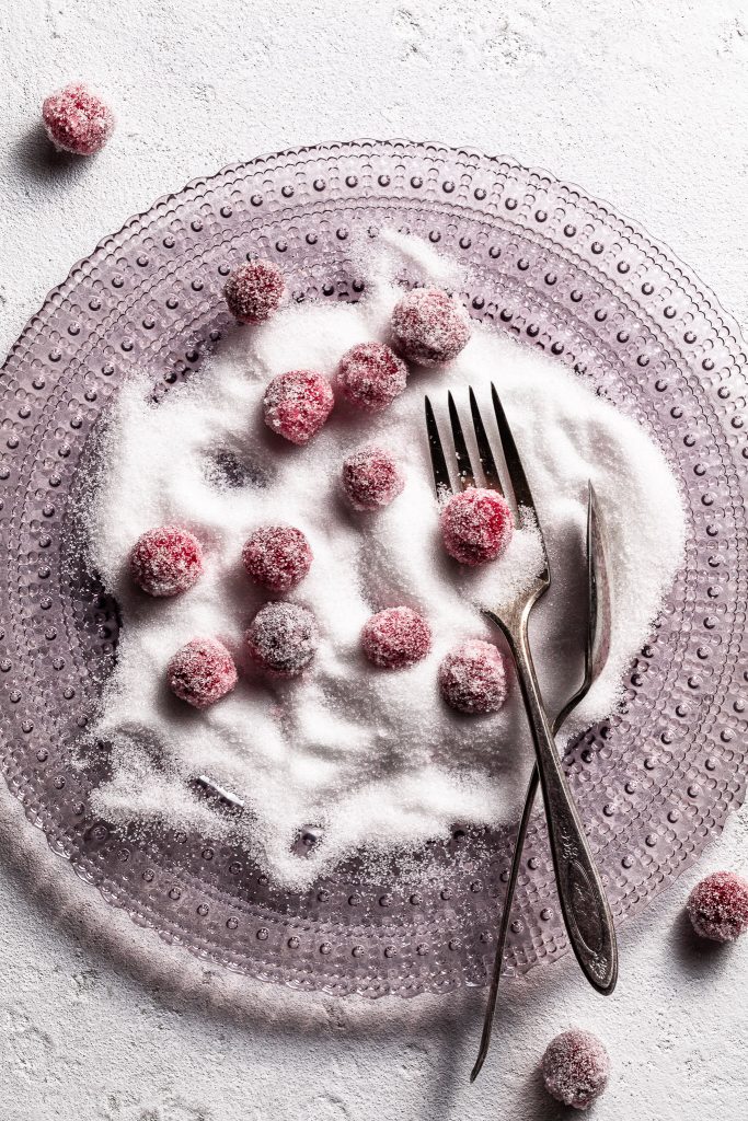 A light purple glass plate covered in granulated sugar in which cranberries have been rolled and covered.