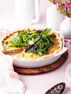 A quiche in a white tart dish with a slice served. White vases are in the background on this brunch table.