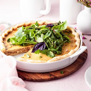 A quiche in a white tart dish with a slice served. White vases are in the background on this brunch table.