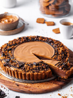A Vegan chocolate biscoff tart with one slice cut and partly removed to reveal the inside of the tart showing off the chocolate layer topped with cookie butter.