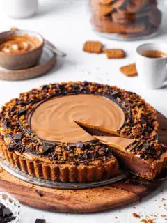 A Vegan chocolate biscoff tart with one slice cut and partly removed to reveal the inside of the tart showing off the chocolate layer topped with cookie butter.