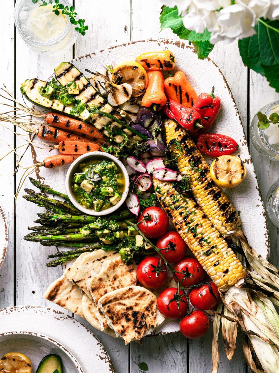 A white platter filled with grilled vegetables covered in avocado chimichurri sauce.