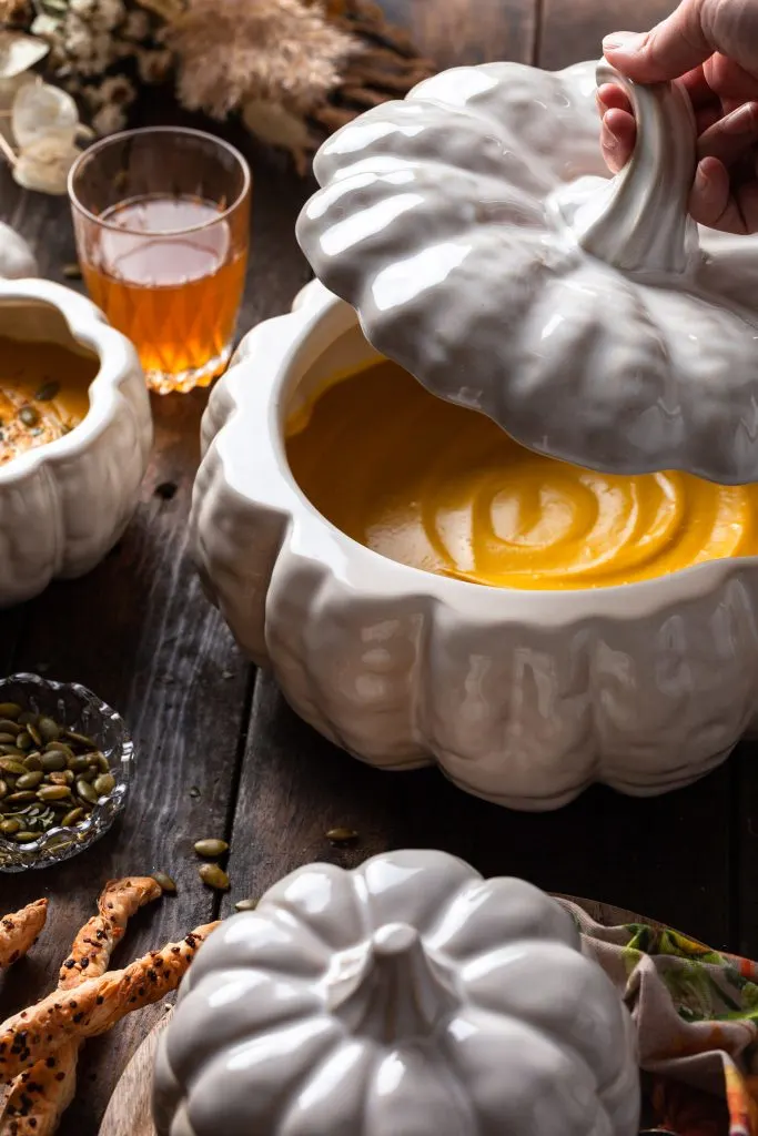 A white pumpkin terrine filled with creamy roasted pumpkin soup on a harvest table. 