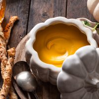 A white pumpkin shaped bowl filled with creamy roasted squash soup.