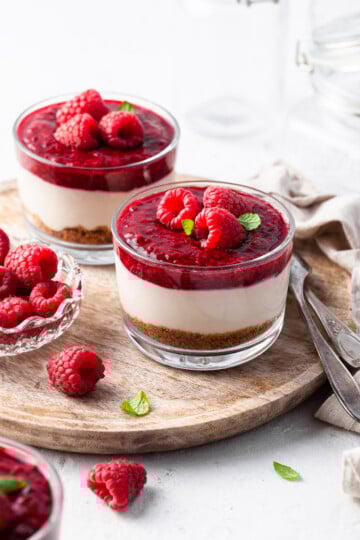 No Bake Vegan Cheesecake Jars garnished with raspberries, served on a wooden tray