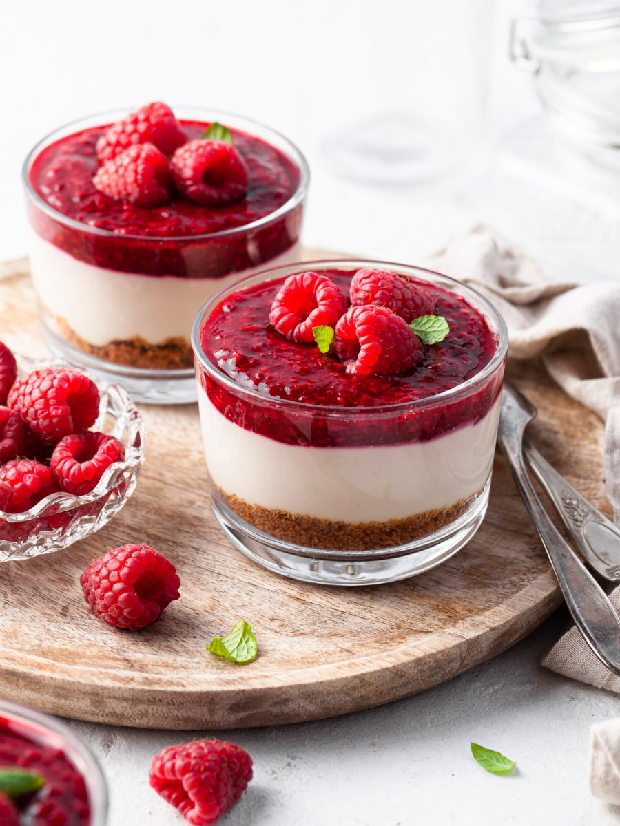 No Bake Vegan Cheesecake Jars garnished with raspberries, served on a wooden tray
