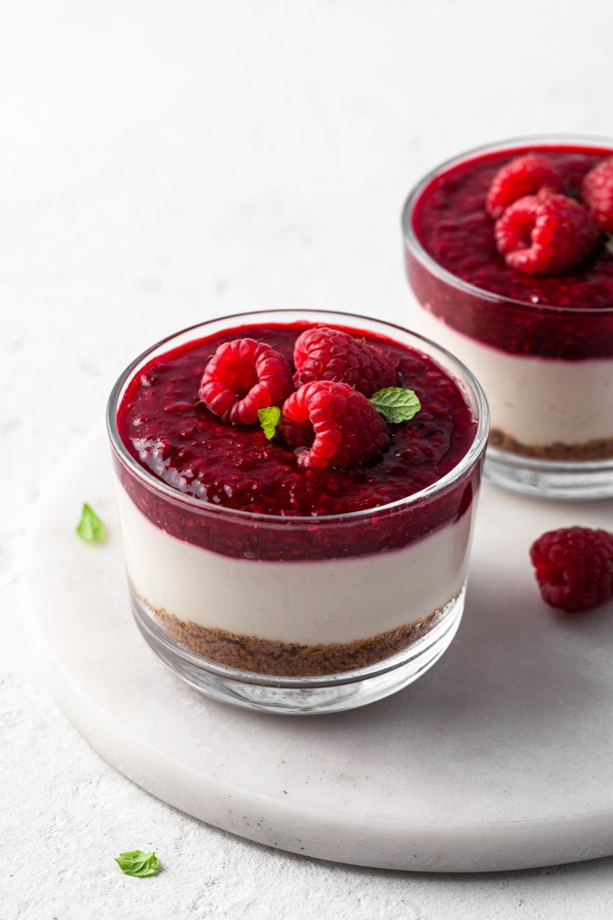 Two jars of non bake dairy free cheesecake cups on a white marble plate