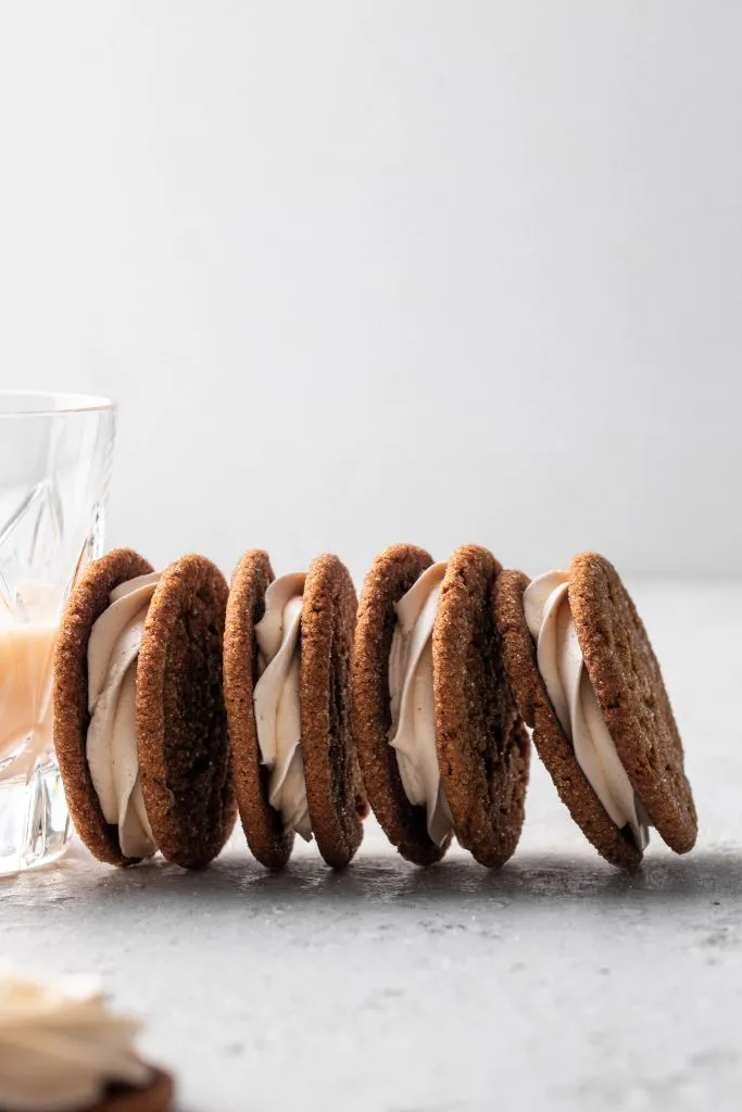 Molasses sandwich cookies leaning on a glass of eggnog