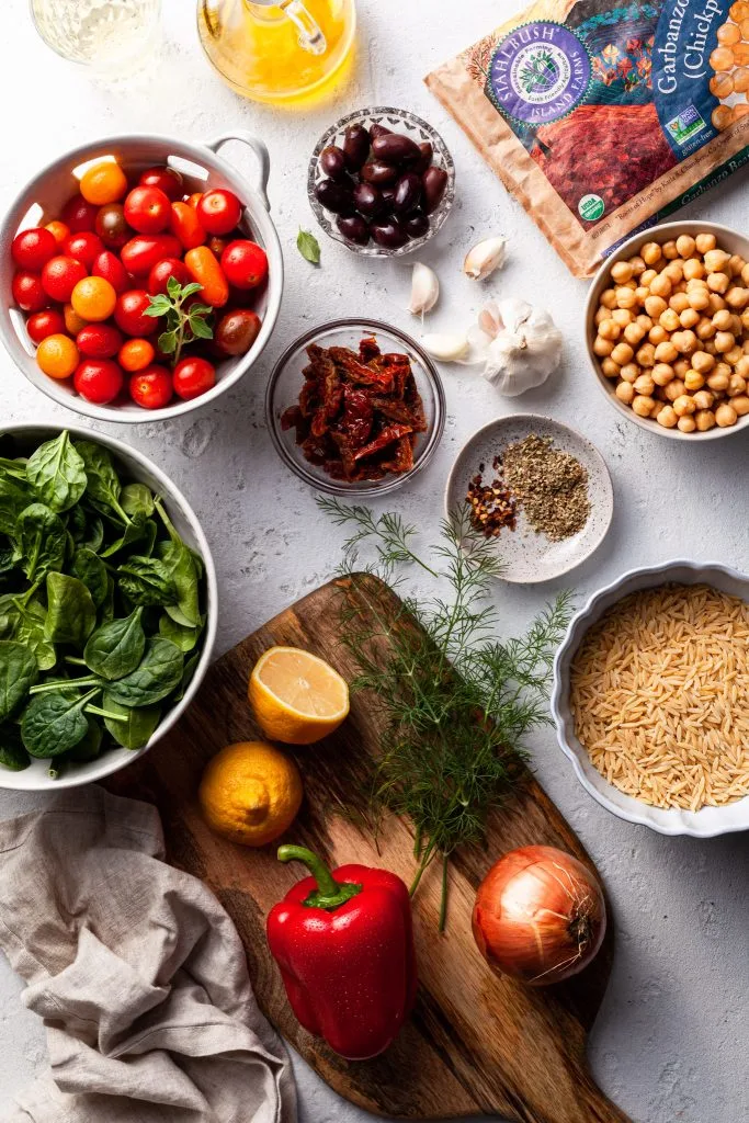 The ingredients for the Greek orzo and chickpeas, including a variety of fresh vegetables, herbs, olive oil and pasta. 