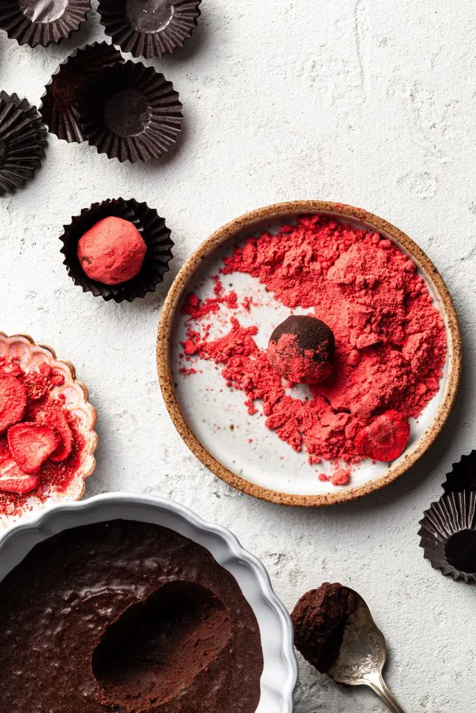 A light blue plate filled with crushed freeze dried strawberries with a chocolate truffle partially covered. 