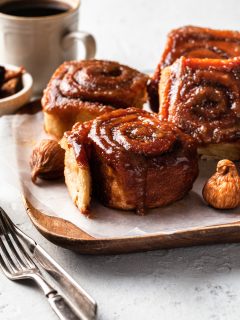 Four sticky buns on a paper lined wooden tray.
