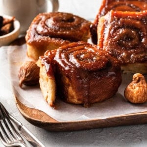 Four sticky buns on a paper lined wooden tray.