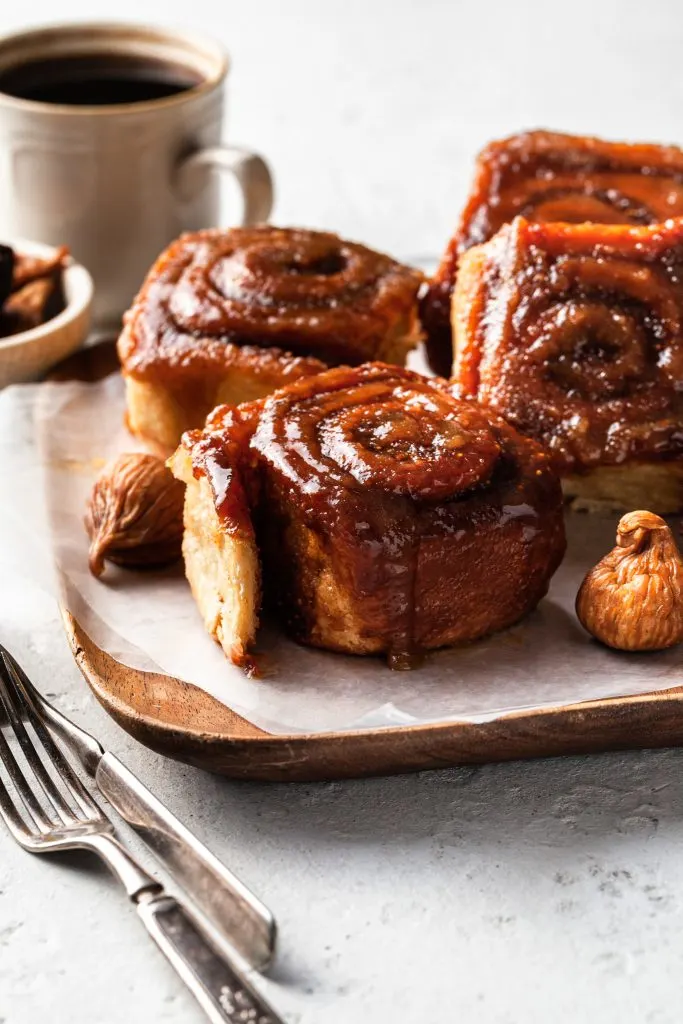 Four sticky buns on a paper lined wooden tray.