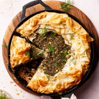 A cast-iron pan filled with a spanakopita, with 2 slices cut and one missing.