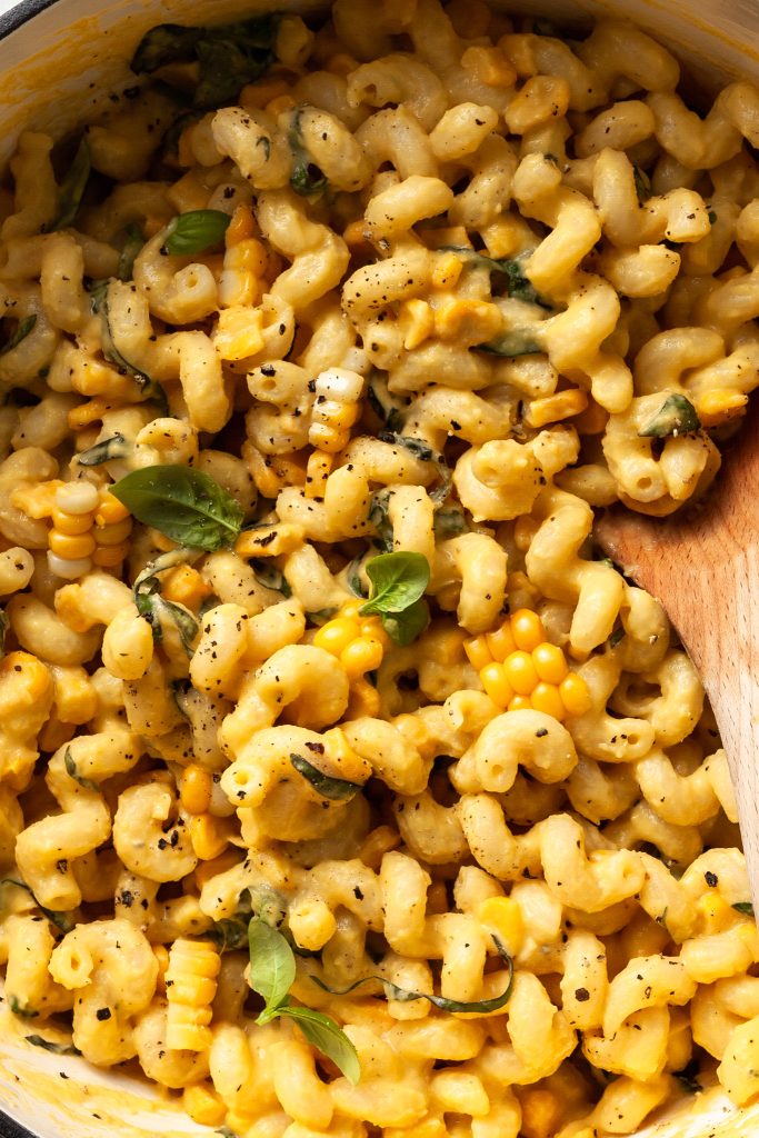 Close up of curly noodles covered in a light yellow cream sauce dotted with corn kernels and basil leaves. 