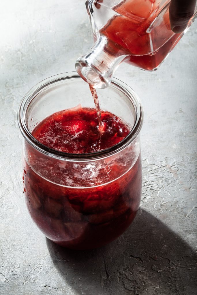 Red wine vinegar being poured into a crushed berries in a glass canister.