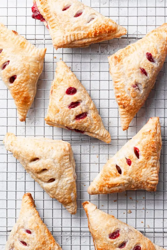 View looking down on triangle shaped hand pies on a wire cooling rack, some which have a little red berry filling leaking out. 