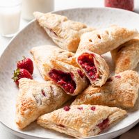 Strawberry turnovers in a curved cream colored platter. One turnover has been cut in half to reveal the red fruit center.