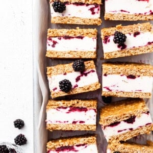 Baking tin lined with white parchment, filled with ice cream sandwiches that contain and purple swirl through the white ice cream layer.