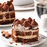 A serving of tiramisu missing a bite on a white plate beside a gingerbread cookie.
