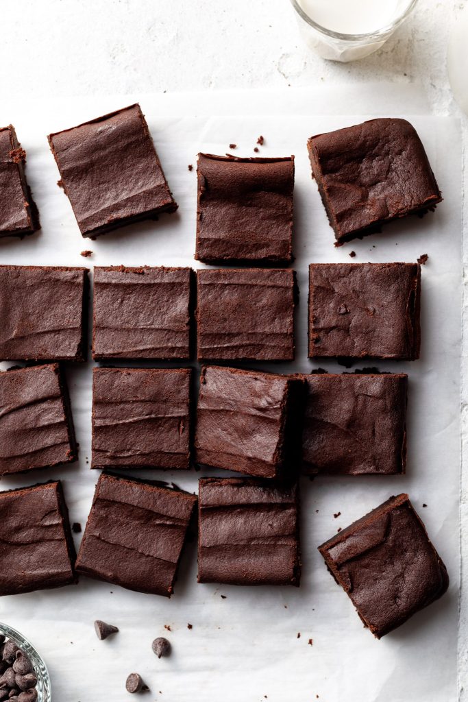 A batch of brownies sliced into evenly sized squares on a sheet of parchment paper. 