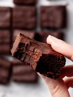 View of someone holding a brownie with a bite missing, over a batch of brownies.